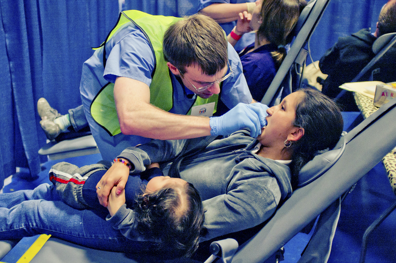 A patient holds a child on her lap while receiving treatment from second-year dental student Brendan Dolan